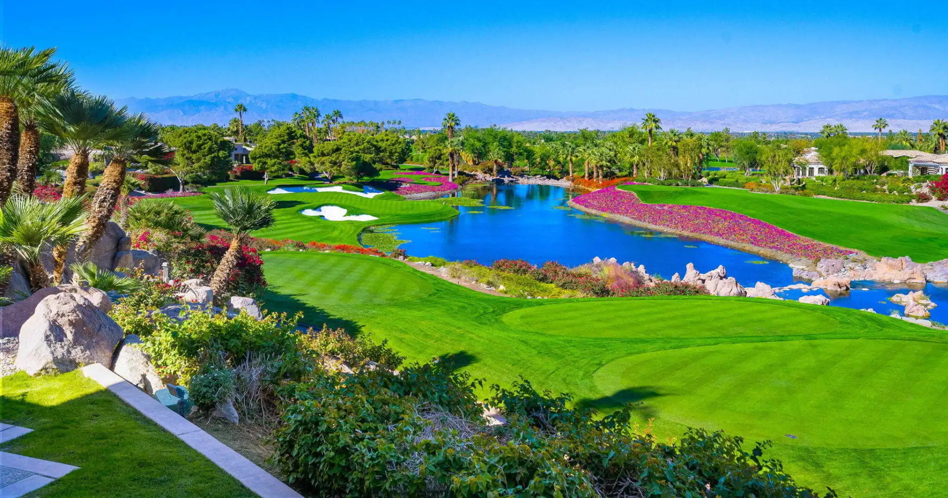 The Vintage Club golf course in Indian Wells with lush fairways, colorful landscaping, water features and dramatic mountain views.