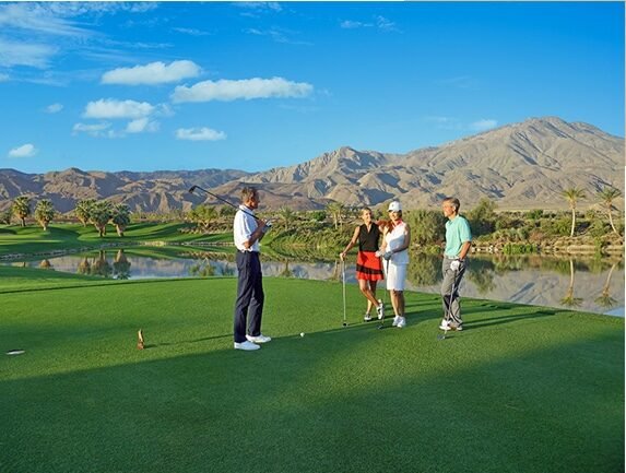 Golfers at Andalusia Country Club in La Quinta, California, with a lake, lush fairways and dramatic Santa Rosa Mountain views.